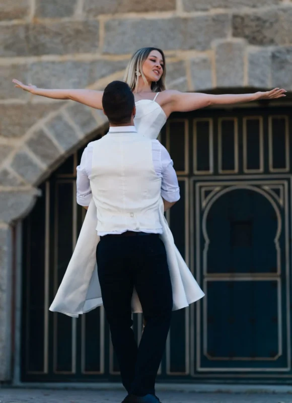 Novio alzando a la novia con los brazos abiertos en una figura de exhibición, ideal para bailes de boda