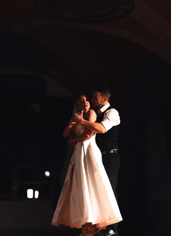 Pareja de novios en posición de baile cerrada, interpretando una coreografía elegante de bailes de boda en interior.