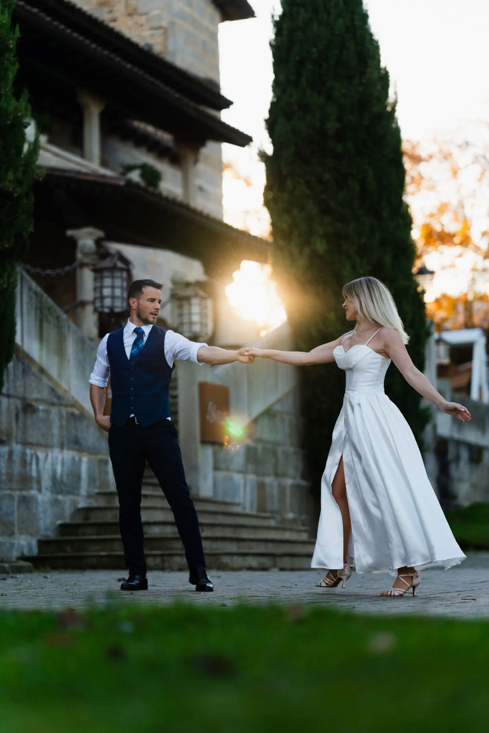 Bailes de boda al atardecer frente a una finca de piedra, con el sol detrás
