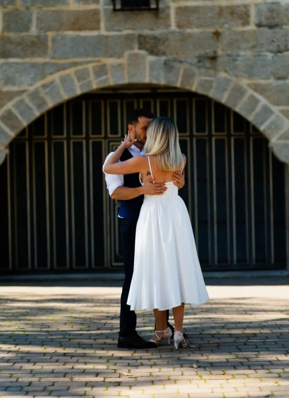 Novios abrazados en baile de boda frente a un arco de piedra
