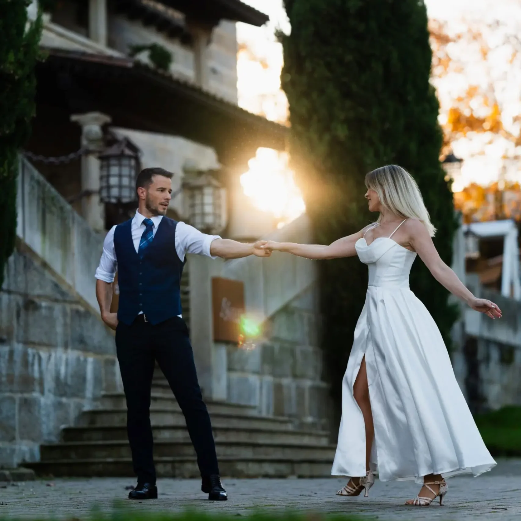 Bailes de boda al atardecer frente a una finca de piedra, con el sol detrás